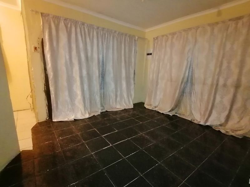 An empty living room featuring dark tiled flooring and sliding glass doors, requiring minor cosmetic repairs to the wall plaster.