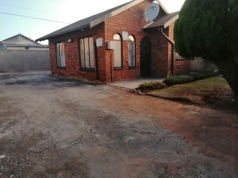 Front view of a face brick house featuring arched windows, a tiled roof, and an unpaved driveway area.