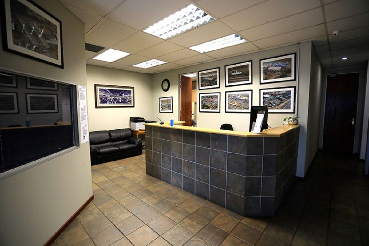 A professional commercial reception area featuring a tiled reception desk, durable floor tiling, and recessed lighting within a suspended ceiling system.
