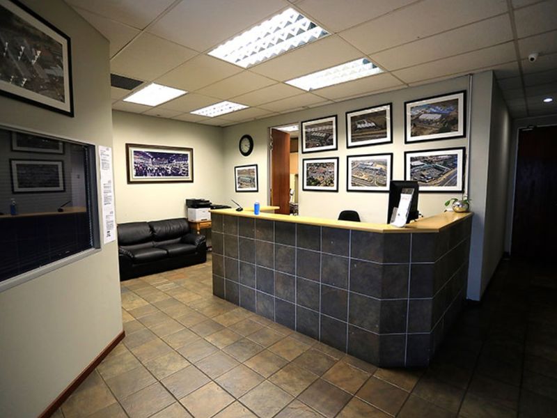 A professional commercial reception area featuring a tiled reception desk, durable floor tiling, and recessed lighting within a suspended ceiling system.