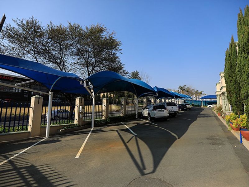 Commercial parking area featuring multiple blue shade cloth structures, asphalt paving, and secure perimeter fencing.
