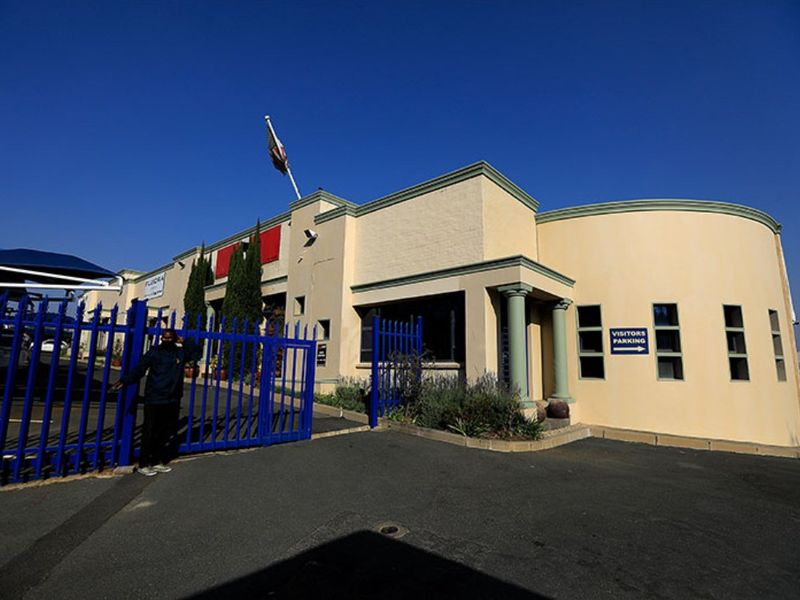 Front exterior view of a commercial property featuring a curved facade, decorative columns, and a secure gated entrance with asphalt driveway.
