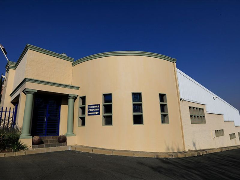 Front exterior view of a commercial building featuring a distinctive curved facade, decorative columns, and a paved visitor parking area.