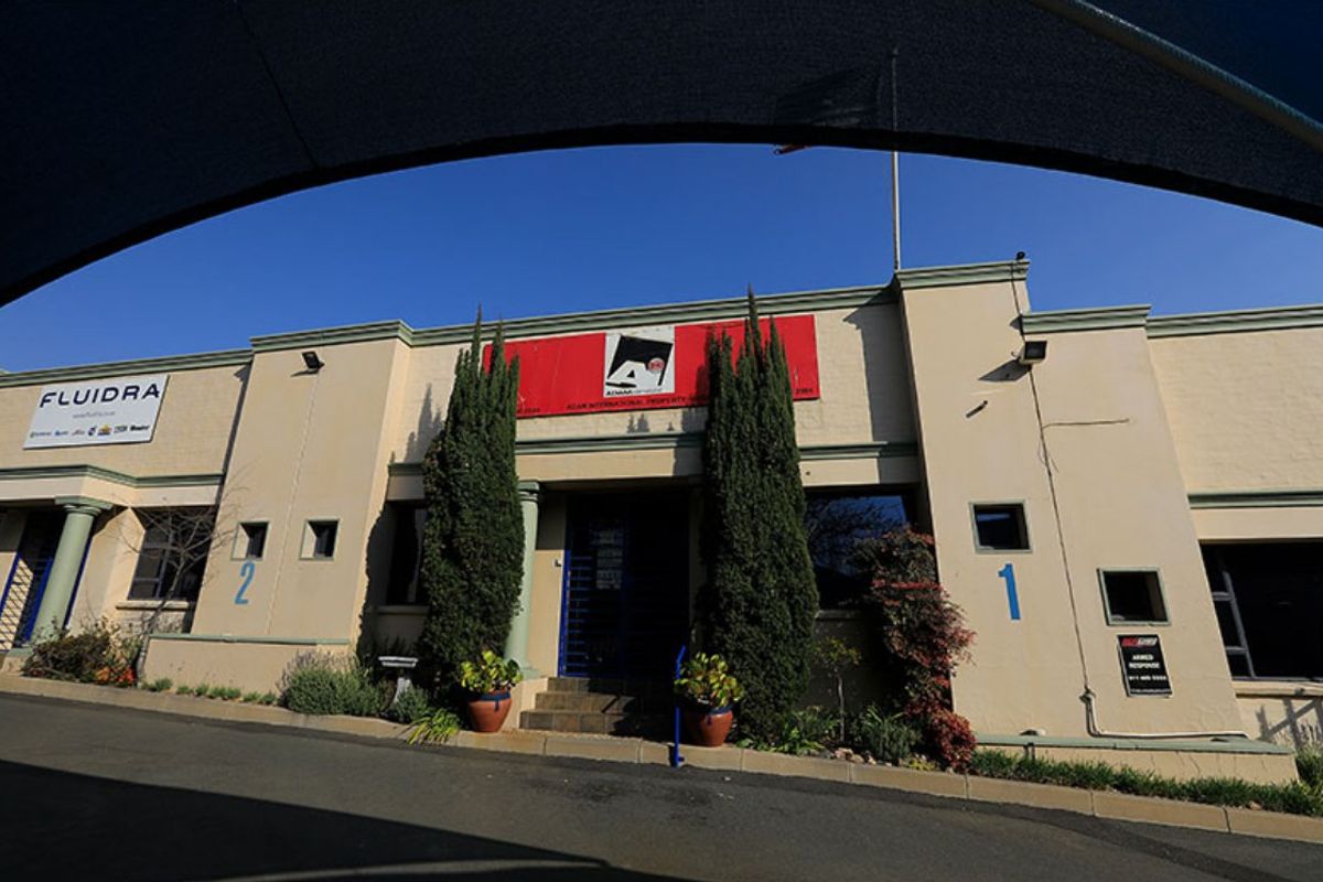 Front facade of a commercial property featuring prominent signage, security access, and paved driveway access with established landscaping.