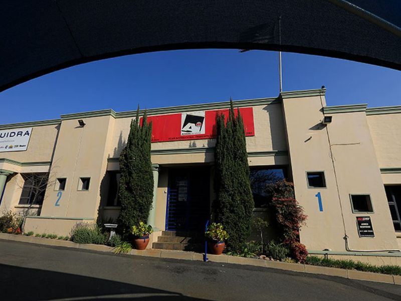 Front facade of a commercial property featuring prominent signage, security access, and paved driveway access with established landscaping.