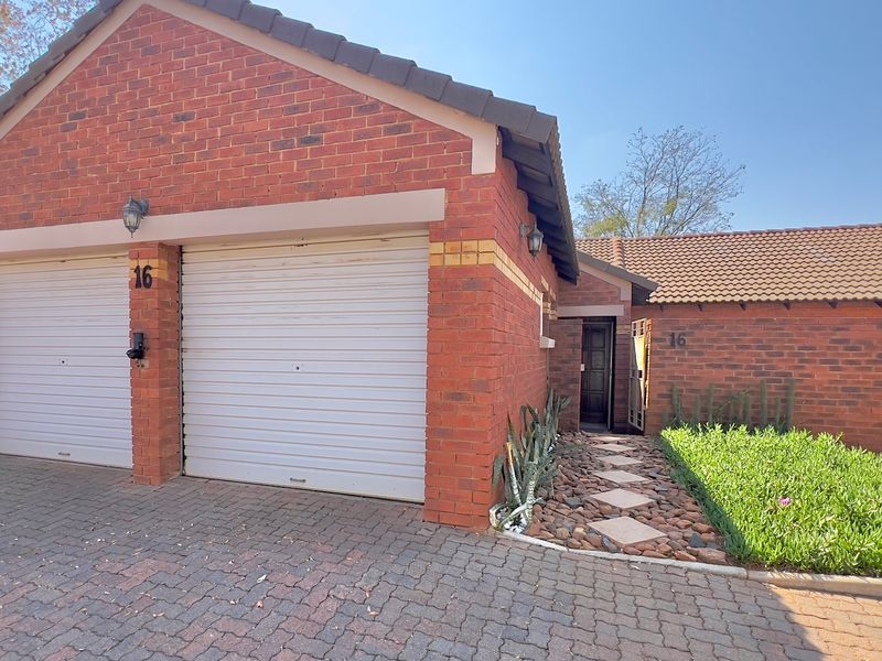 Front view of a townhouse featuring a double garage with roller doors, brick exterior, and a paved driveway with a stone walkway leading to the entrance.