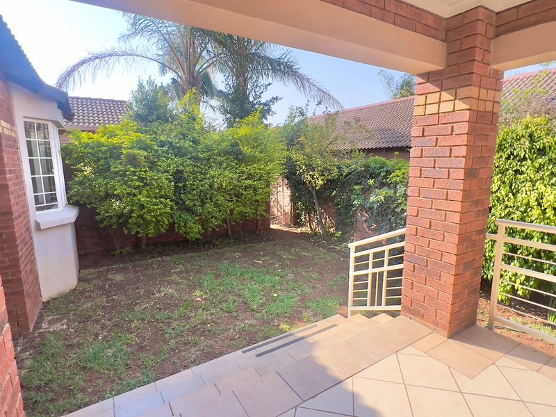 Covered patio area with brick pillars and tiled flooring, overlooking a private garden space with established greenery.