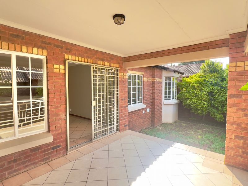 A covered patio area featuring tiled flooring, exposed brickwork, and a security gate providing access to the interior of the townhouse.