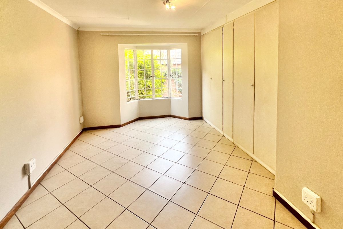 A bright, empty bedroom featuring tiled flooring, a classic bay window, and extensive built-in cupboard storage.