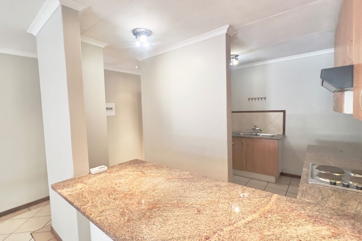A functional kitchen featuring granite countertops, built-in cabinetry, an electric hob with extractor fan, and tiled flooring in a neutral setting.