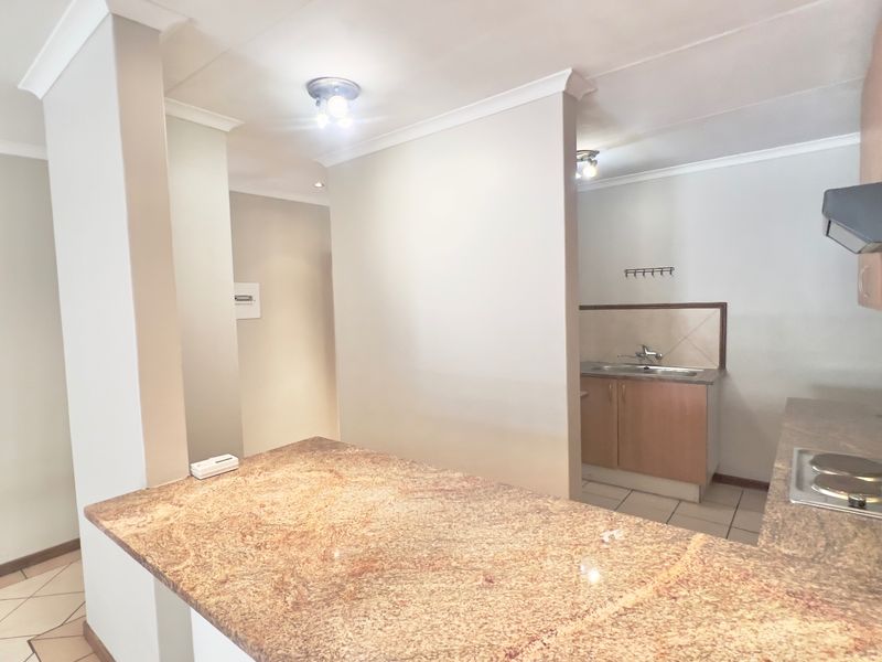 A functional kitchen featuring granite countertops, built-in cabinetry, an electric hob with extractor fan, and tiled flooring in a neutral setting.