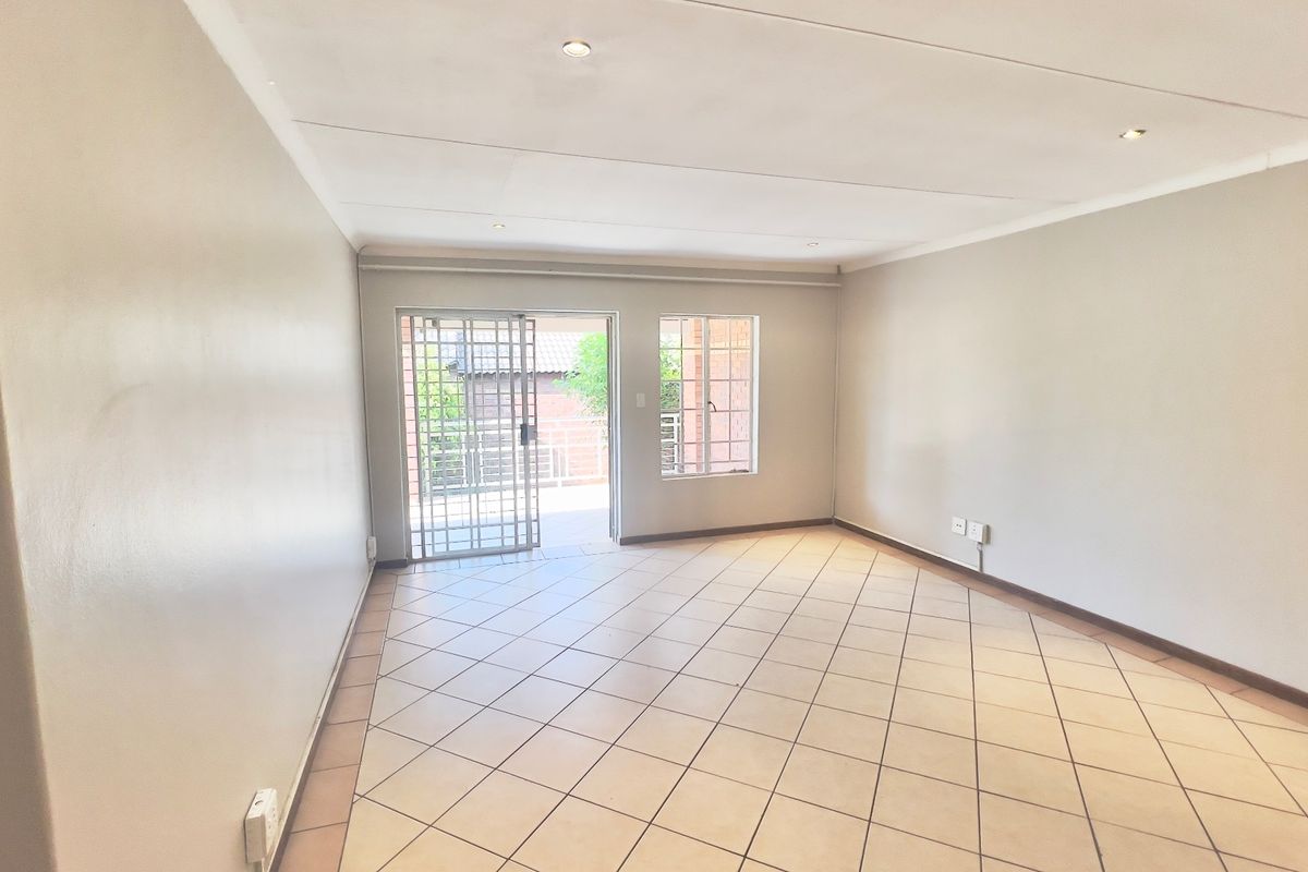 A bright, empty living room featuring neutral walls, tiled flooring, recessed lighting, and direct access to an outdoor area through a security gate.