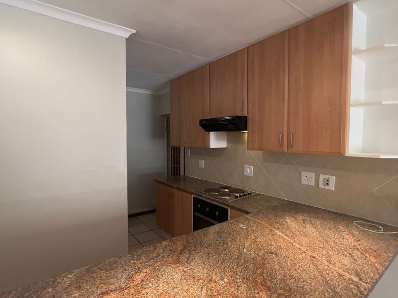 Functional kitchen featuring granite countertops, built-in oven, electric hob, and ample laminate cabinetry, offering a practical layout for culinary activities.