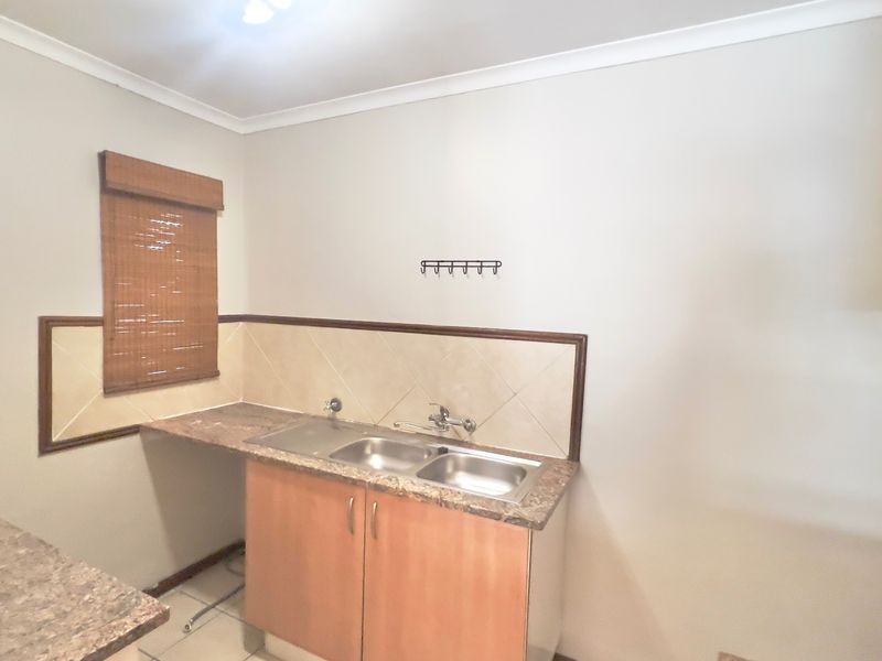 A functional scullery area featuring a double bowl stainless steel sink, laminate countertops, and tiled splashback with timber cabinetry.