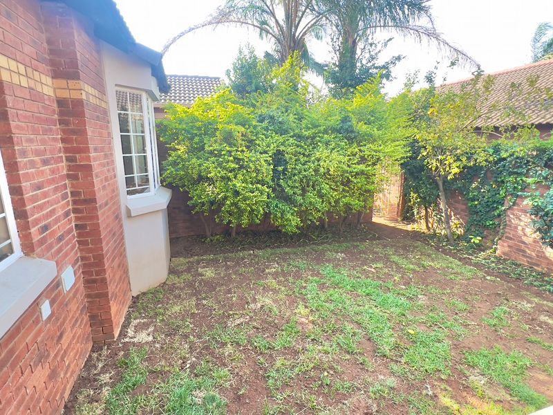 A private rear garden area featuring a brick townhouse facade, bay window, and established perimeter walling with mature greenery.