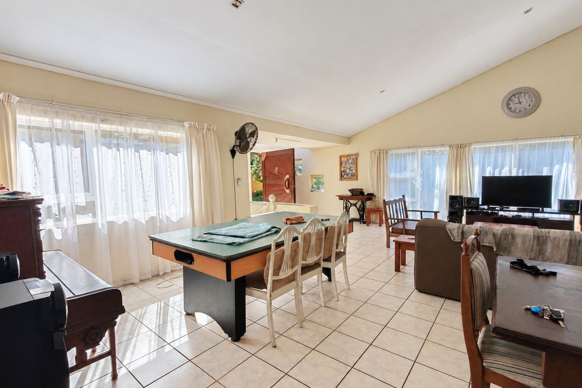 Spacious living area featuring tiled flooring, a vaulted ceiling with recessed lighting, and large windows providing ample natural light.