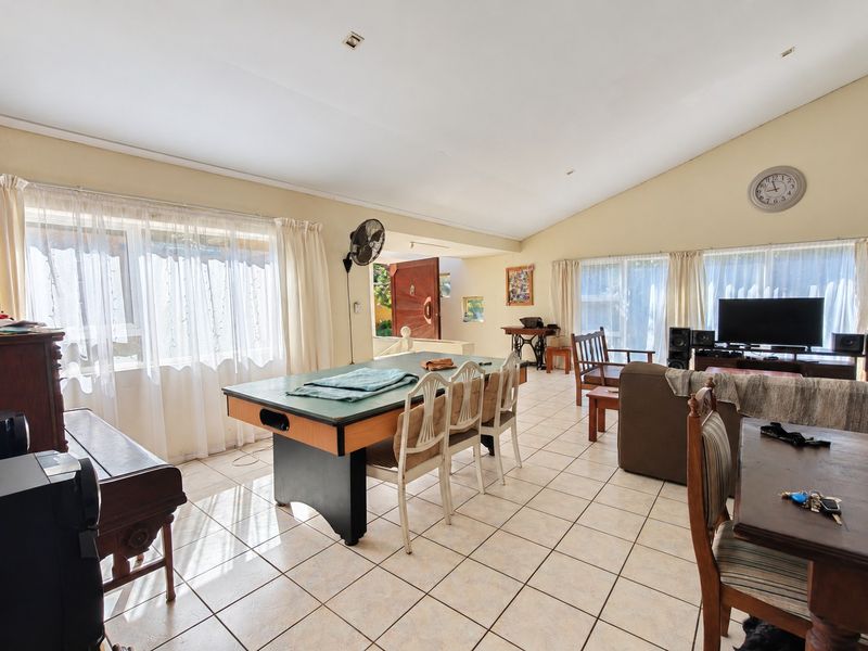 Spacious living area featuring tiled flooring, a vaulted ceiling with recessed lighting, and large windows providing ample natural light.