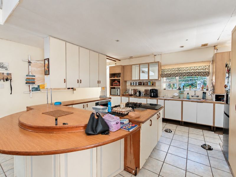 Spacious kitchen featuring extensive built-in cabinetry, a large central island with a gas hob, and tiled flooring, offering significant potential for modernization.