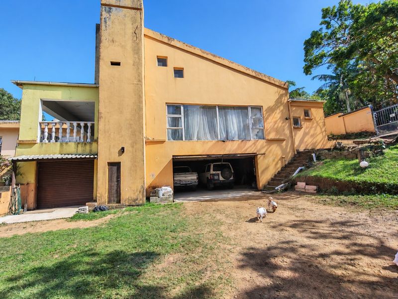 Rear view of the property featuring a garage, an upper-level balcony with balustrades, and a large chimney, showing signs of significant exterior weathering.