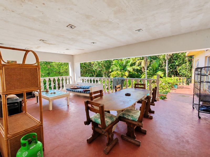Spacious covered patio area featuring a concrete floor, balustrade railing, and recessed lighting, overlooking a lush garden setting.