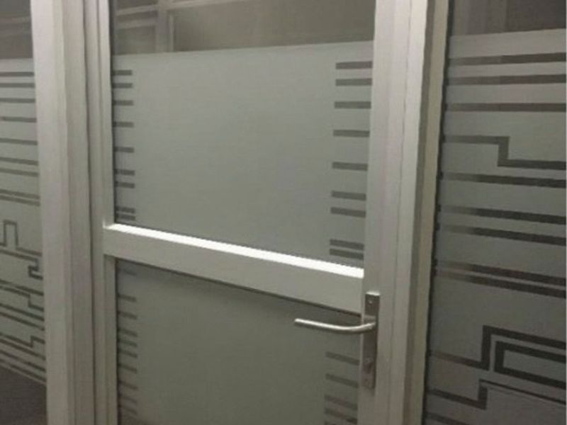 A modern office interior featuring an aluminium-framed glass door with decorative frosted privacy film and professional carpet flooring.