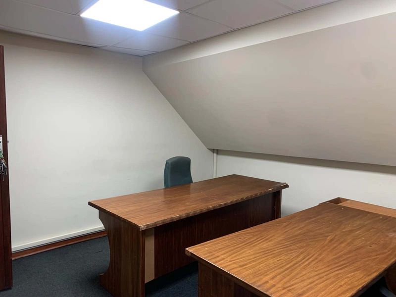 A functional office space featuring a sloped ceiling, recessed lighting, and carpeted flooring, suitable for a professional work environment.