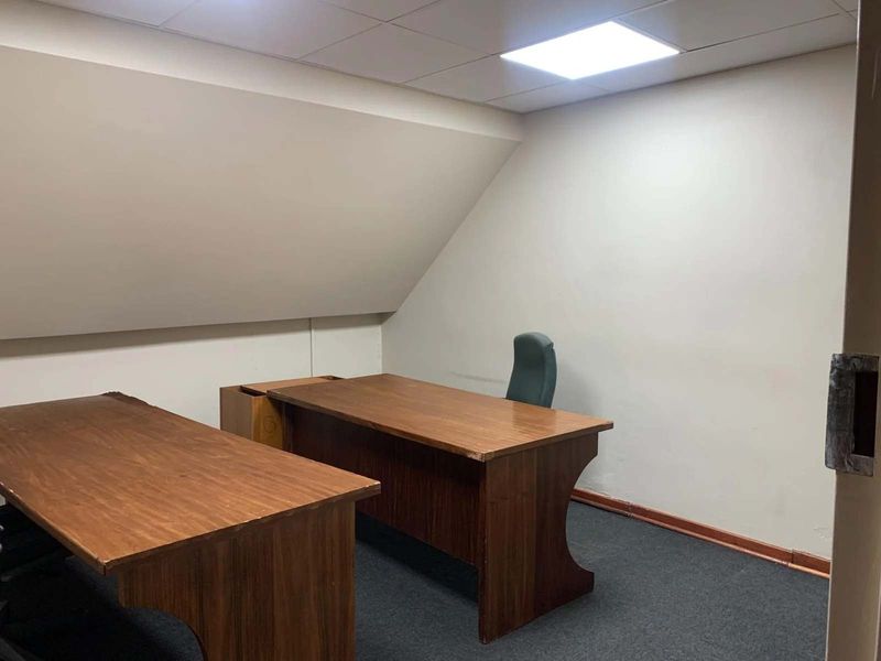 A functional office space featuring a sloped ceiling, recessed lighting, and carpeted flooring, suitable for a professional work environment.