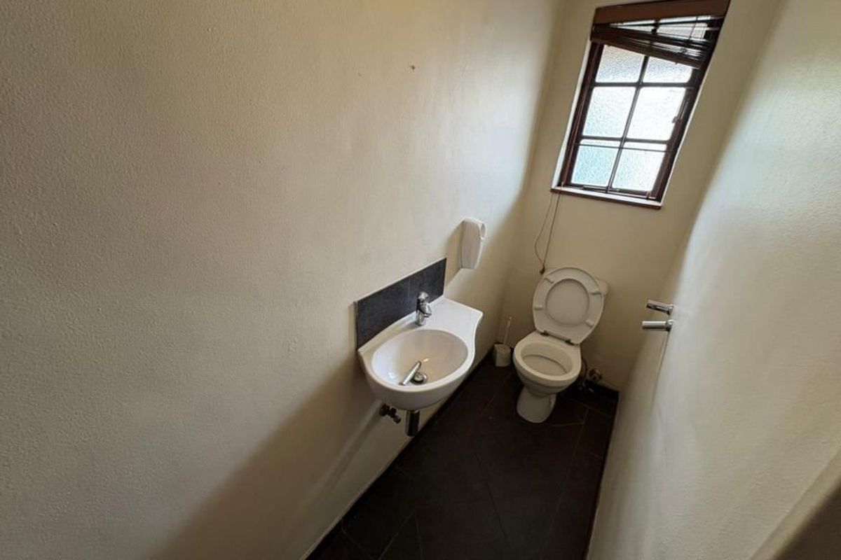 A compact guest bathroom featuring a wall-mounted basin, toilet, and dark tiled flooring, requiring minor cosmetic updates to improve its overall appearance.