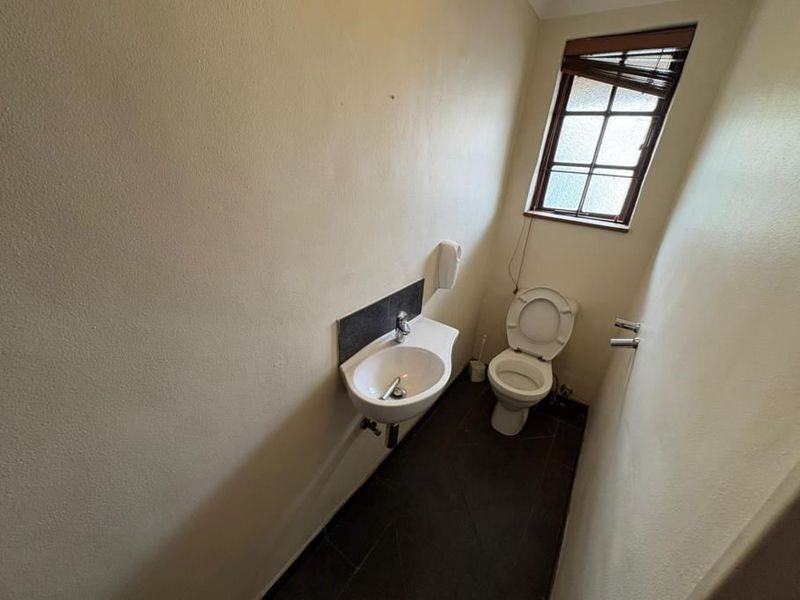 A compact guest bathroom featuring a wall-mounted basin, toilet, and dark tiled flooring, requiring minor cosmetic updates to improve its overall appearance.