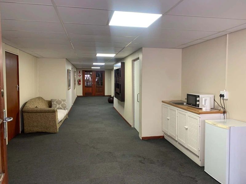 A commercial hallway featuring a drop ceiling, recessed lighting, carpeted flooring, and a small built-in kitchenette area with cabinetry and a sink.