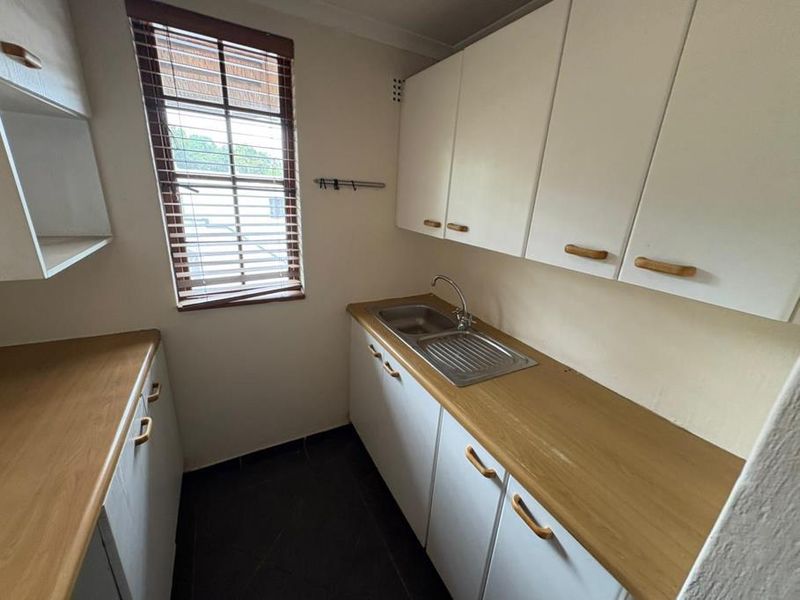 A functional scullery area featuring laminate countertops, built-in cabinetry, and a stainless steel sink, providing practical prep and wash-up space.