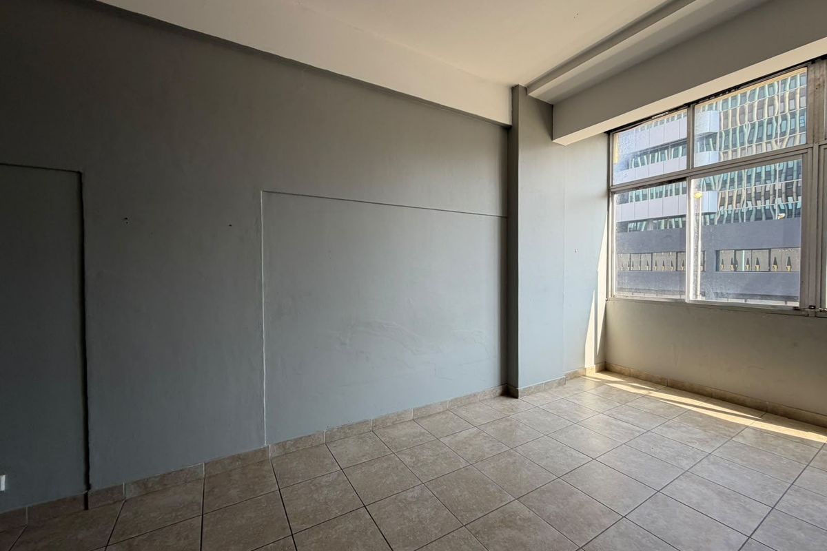 An empty, sunlit living area featuring neutral grey walls and tiled flooring, offering a blank canvas for interior design and personalization.