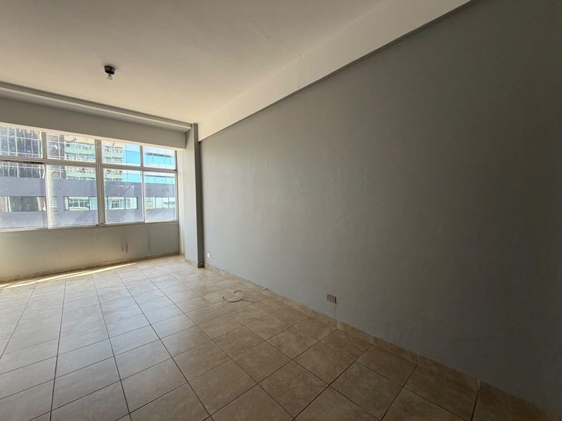 An empty, sunlit living area featuring neutral tiled flooring and large windows, offering a blank canvas ready for personalization and interior design updates.