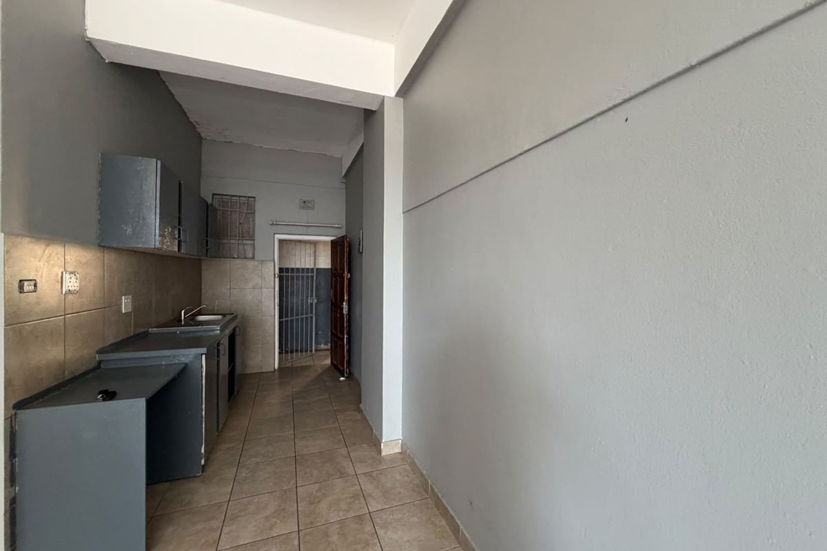 A compact, empty kitchen area featuring built-in cabinetry, a stainless steel sink, tiled backsplash, and tiled flooring, leading to a secure rear entrance.