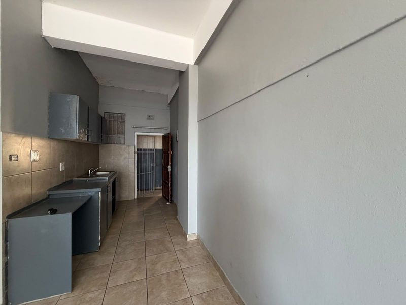 A compact, empty kitchen area featuring built-in cabinetry, a stainless steel sink, tiled backsplash, and tiled flooring, leading to a secure rear entrance.