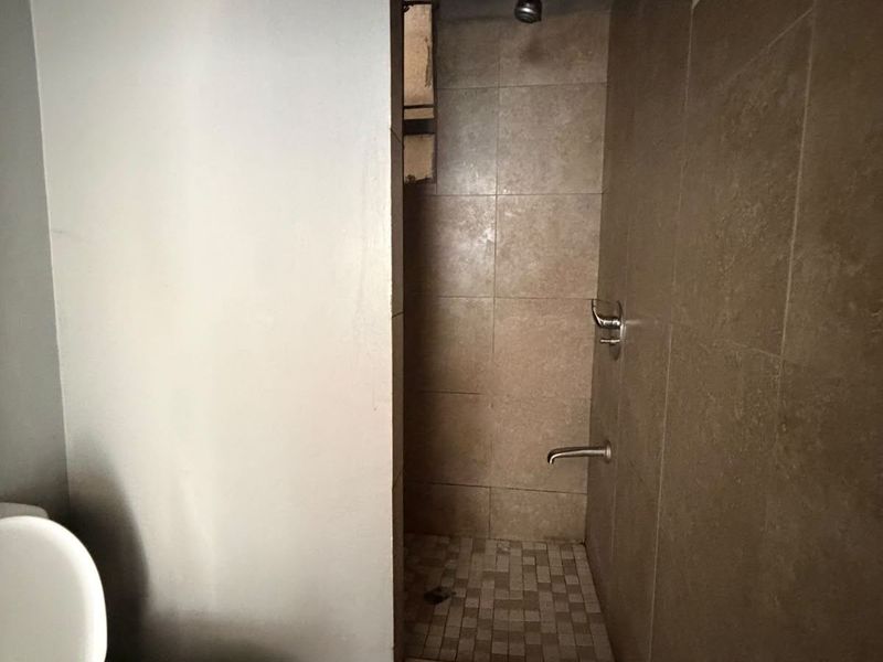 A functional bathroom featuring a tiled shower enclosure and standard toilet, currently in need of cosmetic updates to improve its overall condition.