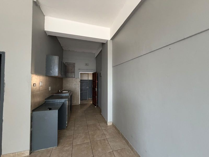 A compact, empty kitchen area featuring tiled flooring, built-in cabinetry, and a stainless steel sink, ready for renovation or modernization.