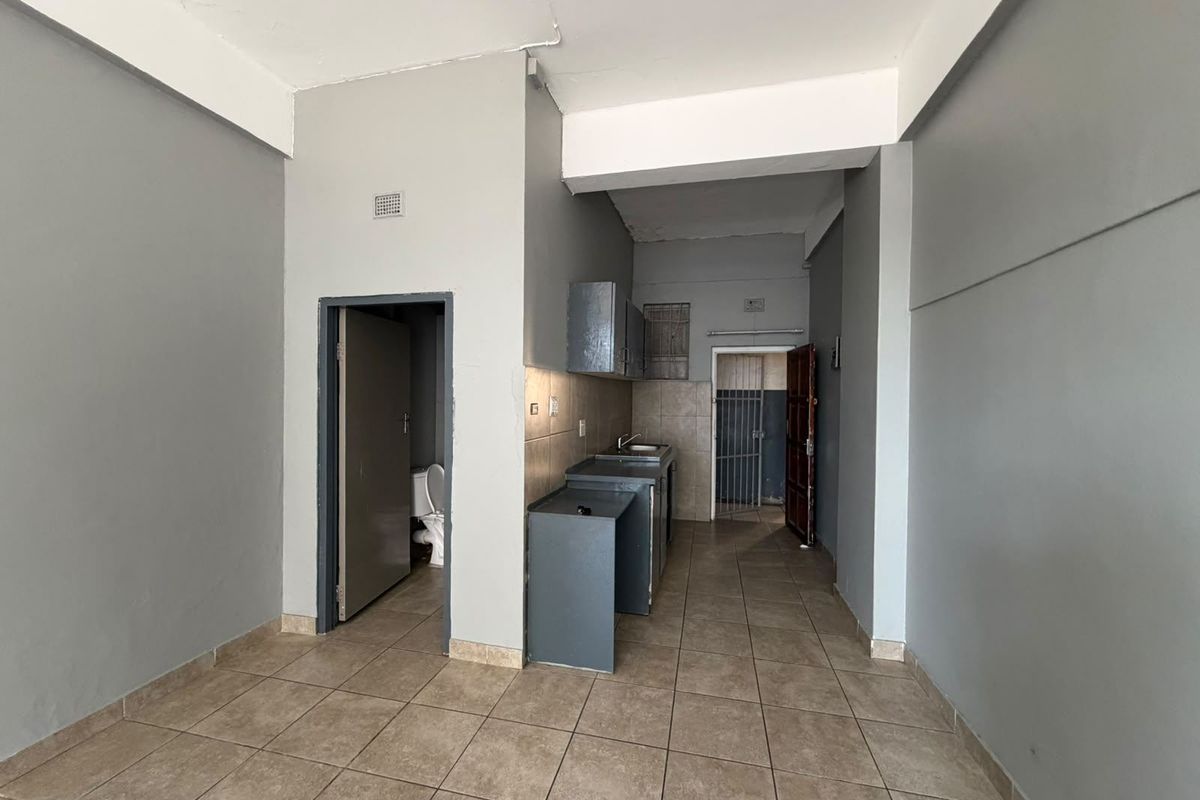 Open plan living area featuring tiled flooring, a compact kitchenette with built-in cabinetry, and access to an adjacent bathroom and secondary entrance.