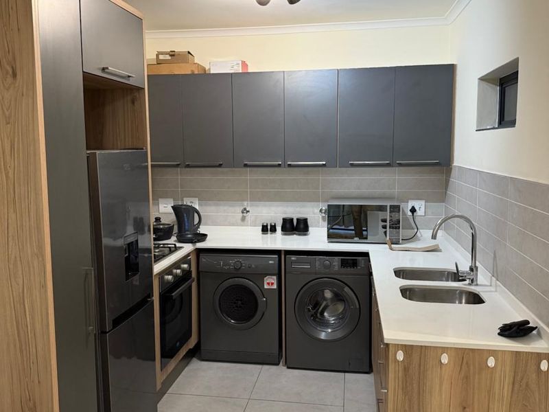 Modern kitchen featuring two-tone cabinetry, stone countertops, tiled backsplash, and integrated laundry appliances, offering a functional and contemporary workspace.