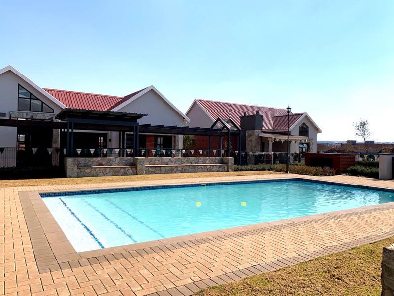 A well-maintained communal swimming pool area featuring a paved deck, stone-clad retaining wall, and a pergola structure set against residential apartment buildings.