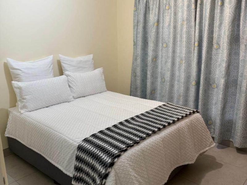 A functional bedroom featuring neutral wall paint, tiled flooring, and window curtain tracks.