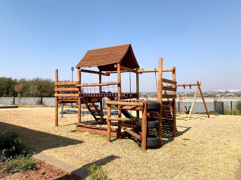 A well-maintained outdoor garden area featuring a wooden jungle gym and swing set, providing a recreational space within the apartment complex grounds.
