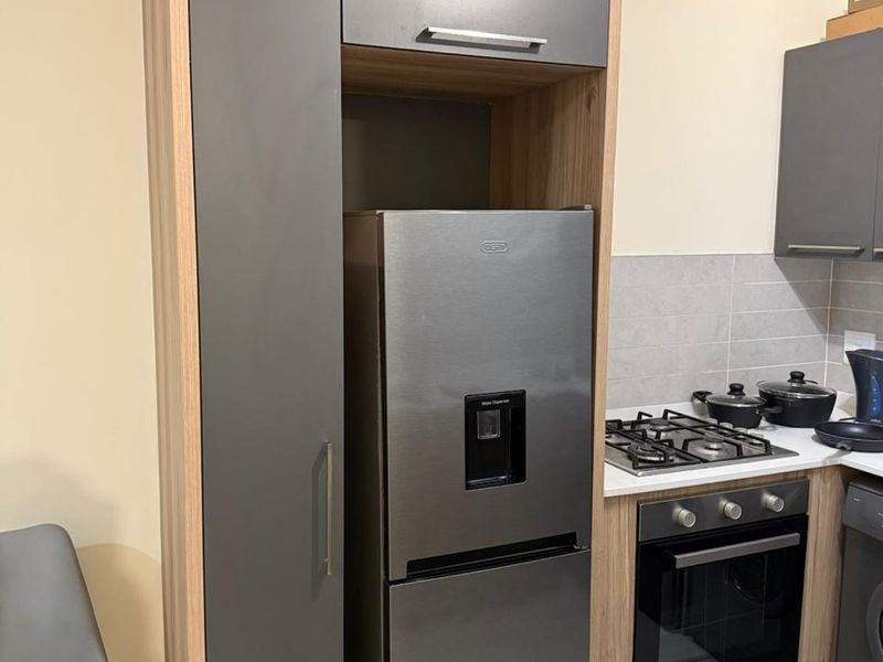 Modern kitchen featuring sleek grey and wood-tone cabinetry, a built-in gas hob, oven, and tiled backsplash.