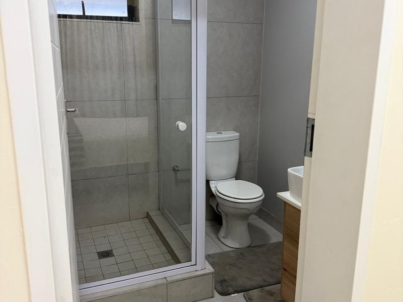A modern bathroom featuring a glass-enclosed shower with a rain shower head, a toilet, and a vanity cabinet with a basin.
