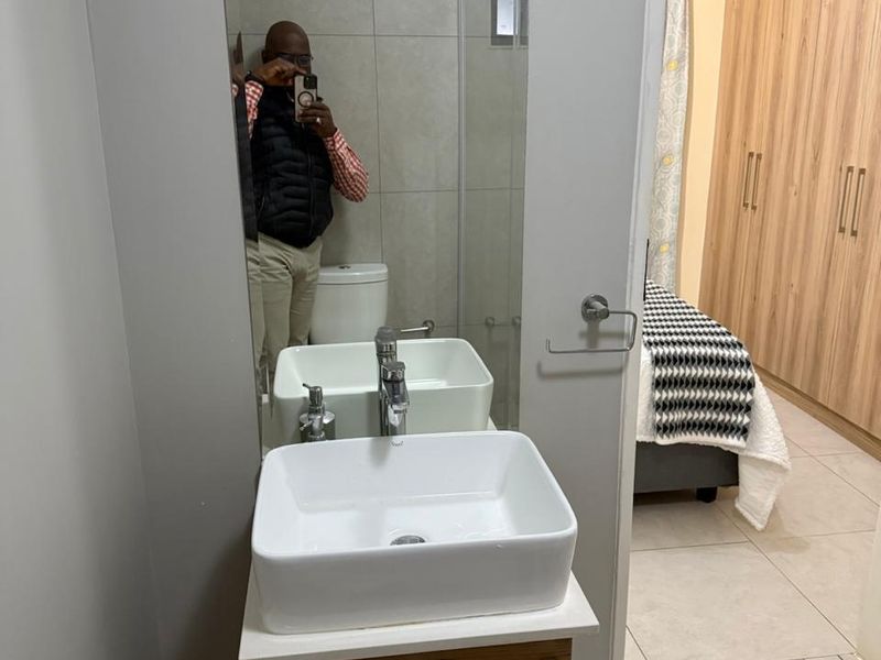 A modern bathroom featuring a vessel sink on a wood-finish vanity, a wall-mounted mirror, and a glass-enclosed shower, with tiled finishes throughout.