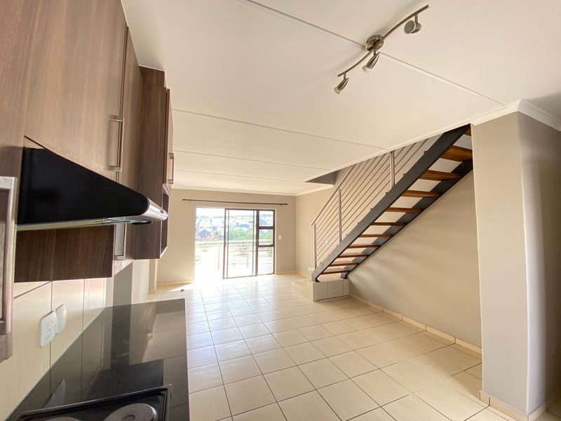 An open-plan living and kitchen area featuring tiled floors, modern cabinetry, and a staircase leading to the upper level with access to a balcony.