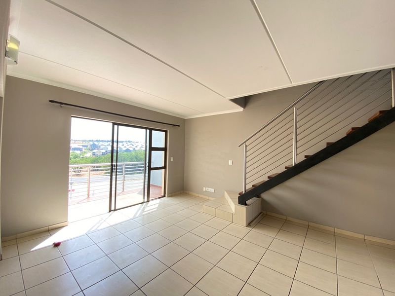 An open-plan living area featuring neutral tiled flooring, a staircase with a modern metal railing, and sliding glass doors leading to a balcony.