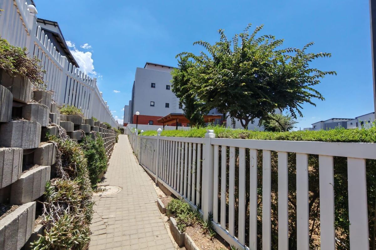 A well-maintained paved walkway bordered by a retaining wall and white picket fencing, leading through the apartment complex grounds.