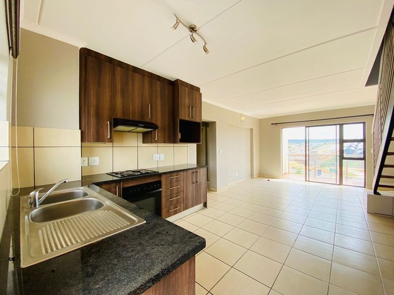 Spacious open-plan kitchen and living area featuring dark wood cabinetry, tiled floors, and sliding doors leading to a balcony with scenic views.
