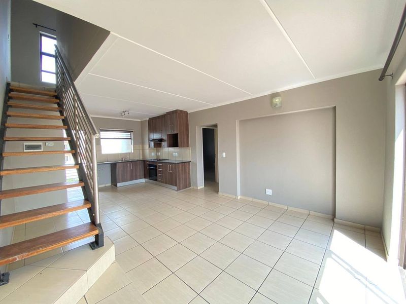 Spacious open-plan living area featuring a modern kitchen with built-in cabinetry, tiled flooring, and an internal staircase leading to the upper level.
